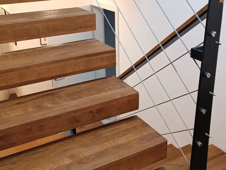 Freitragende Treppe aus Eichenholz mit schwarzem Geländer und Seilbespannung