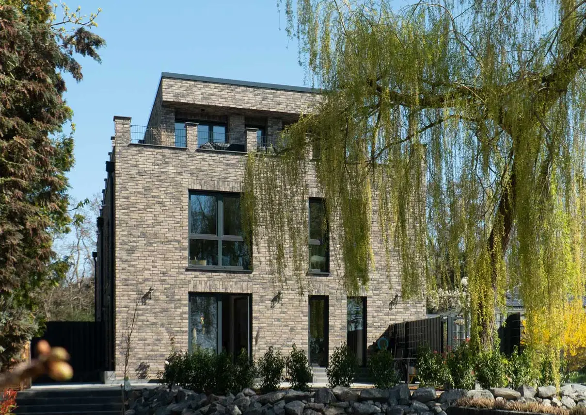 Doppelhaus BS21 mit grauem Klinker und Dachterrasse hinter einer Trauerweide