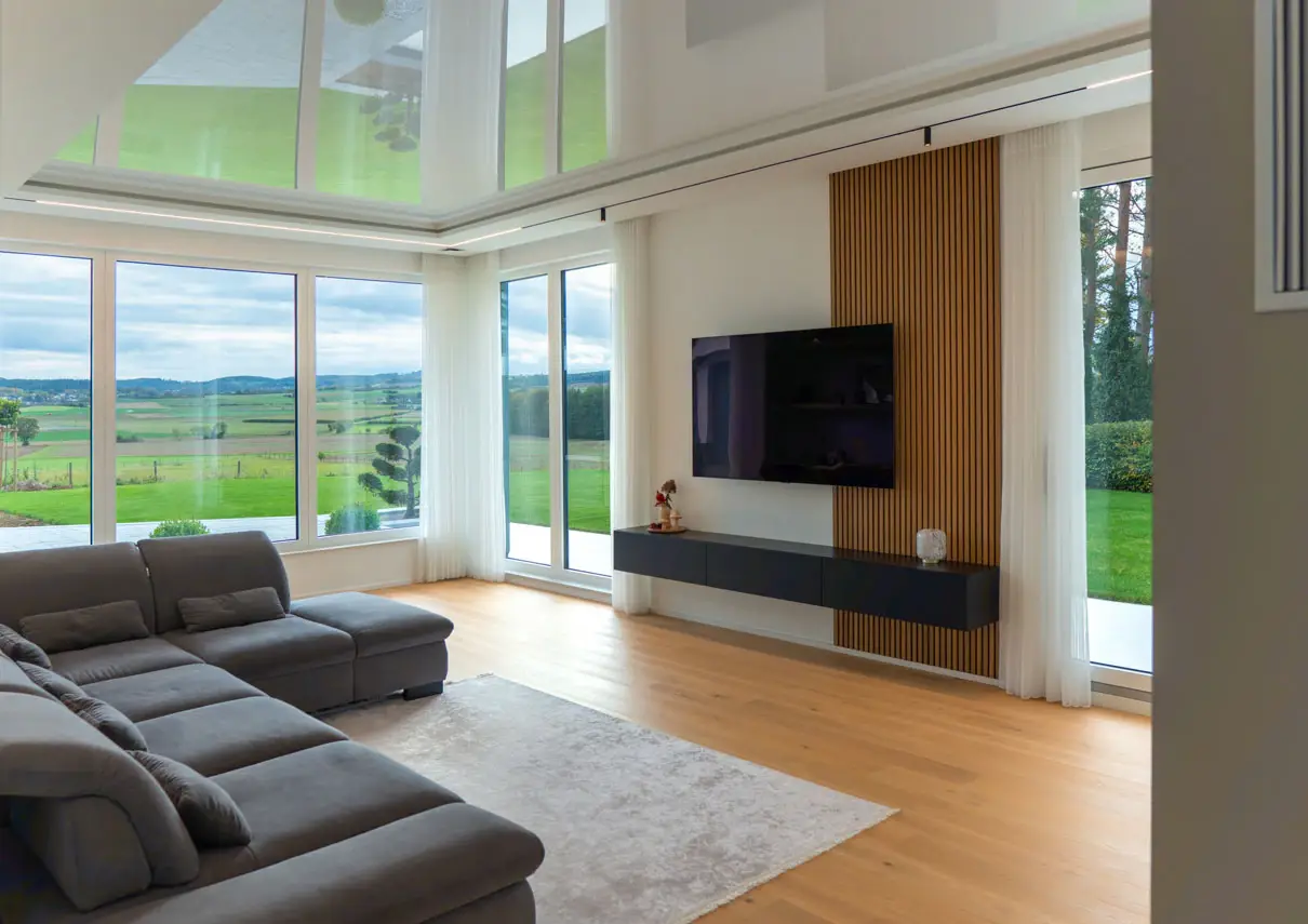 Wohnzimmer mit bodentiefen Panoramafenstern und Blick über die Felder
