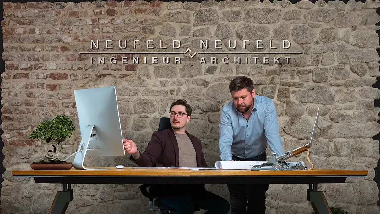 Thomas und Waldemar Neufeld bei einer Planbesprechung vor der Natursteinwand ihres Büros in Blankenheim