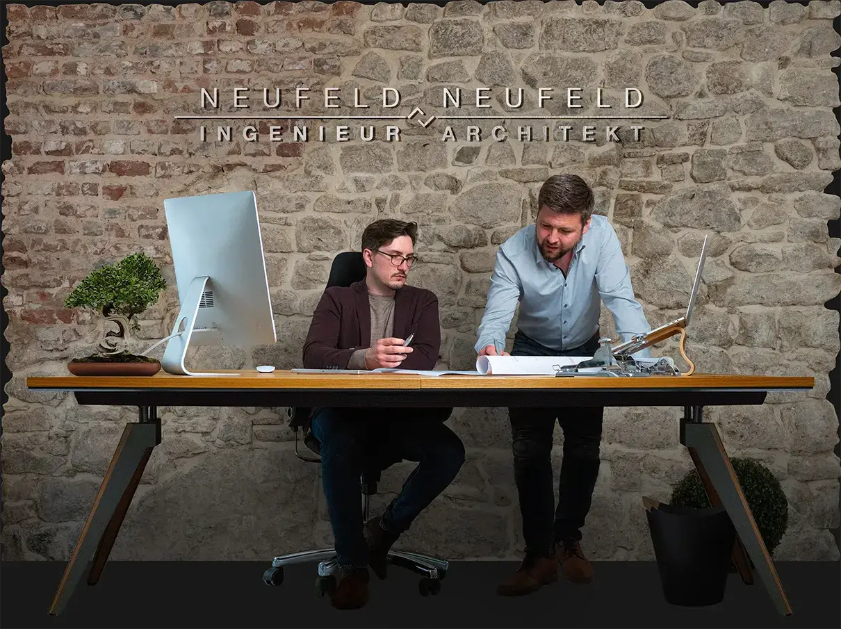Thomas Neufeld und Waldemar Neufeld am Schreibtisch vor der Natursteinwand ihres Büros in Blankenheim